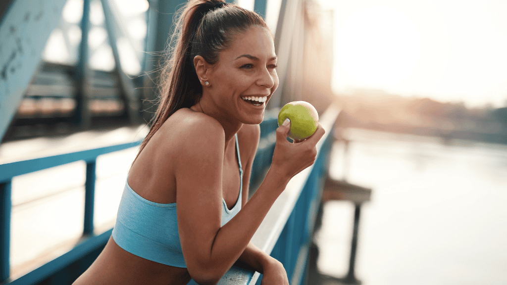 Smiling woman in sportswear holding an apple, representing healthy eating and the importance of macronutrients.