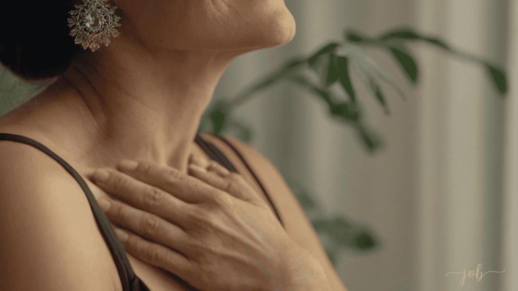 A woman in a serene setting, holding her hands gently on her chest, displaying self-awareness and calmness, with a focus on her elegant earring and subtle background greenery.