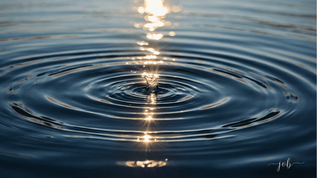 A single droplet of water creating expansive ripples on a serene surface, illuminated by the golden sunlight reflecting the concept of self-awareness.