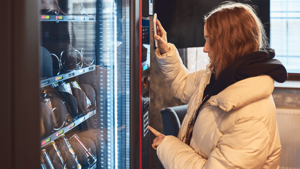 A woman in a winter coat evaluating snack options in a vending machine.