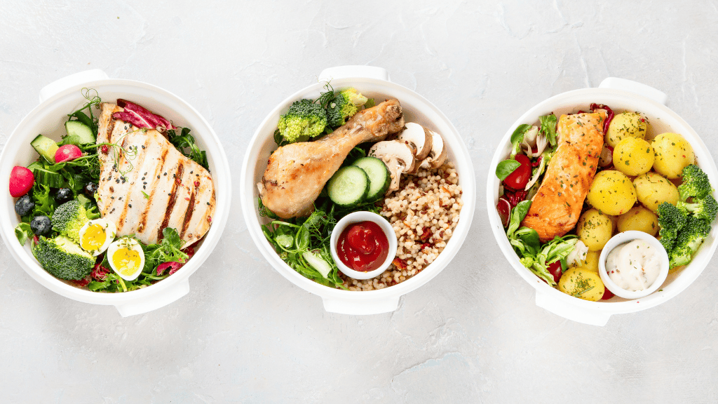 Three bowls filled with nutritious meals including grilled chicken, roasted salmon, and a roasted chicken drumstick with assorted vegetables and grains.