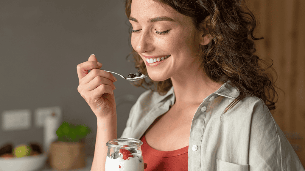 A smiling woman enjoys yogurt with fresh berries, embodying a moment of healthy indulgence.