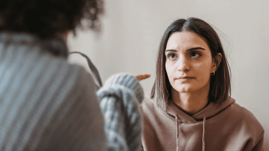 A young woman listens intently, appearing concerned, as another person gestures in conversation, illustrating a difficult discussion.