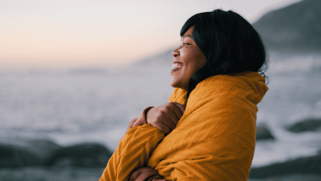 Joyful woman in a yellow jacket laughing by the sea at sunset.