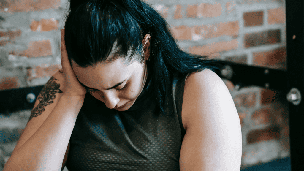 Tired woman resting her head on her hand in a gym, showing signs of fatigue and emotional strain.