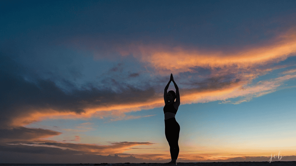 A woman in a yoga pose silhouetted against a vibrant sunset sky, representing balance and body awareness.