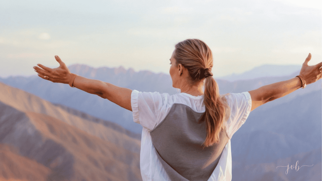 A woman with outstretched arms facing a breathtaking mountain landscape, embracing the vastness and freedom of nature.