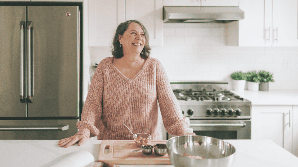 A smiling woman standing in a kitchen, preparing a meal on a cutting board.