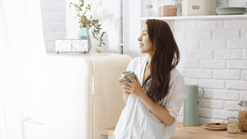 Woman enjoying a peaceful moment in her bright kitchen, reflecting the calm and control gained from meal prepping.