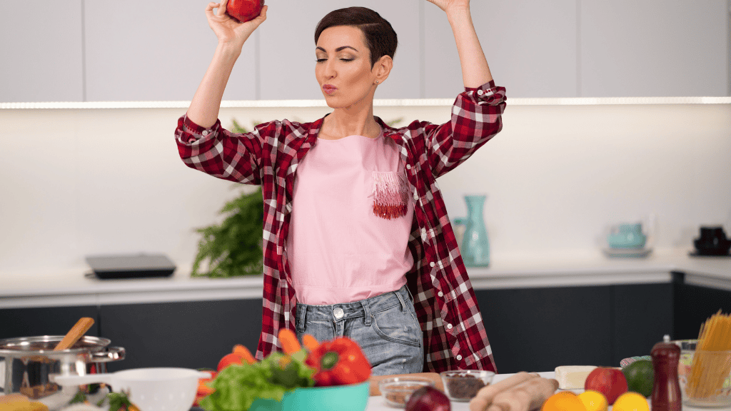 Woman joyfully holding a pomegranate aloft in a modern kitchen filled with fresh produce, celebrating the benefits of meal planning.