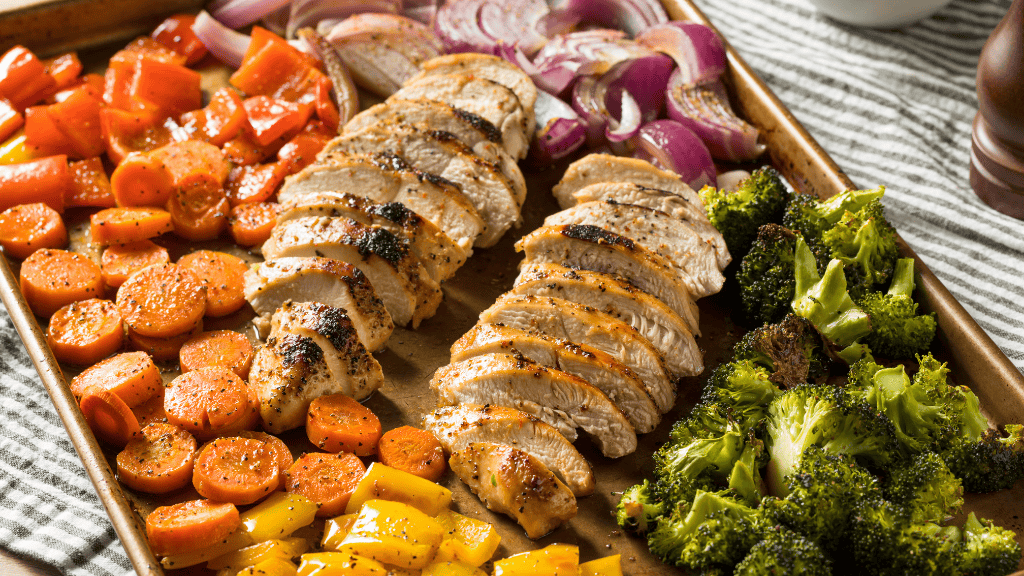 Roasted chicken and assorted vegetables on a baking sheet, showcasing a healthy and efficient batch cooking method.