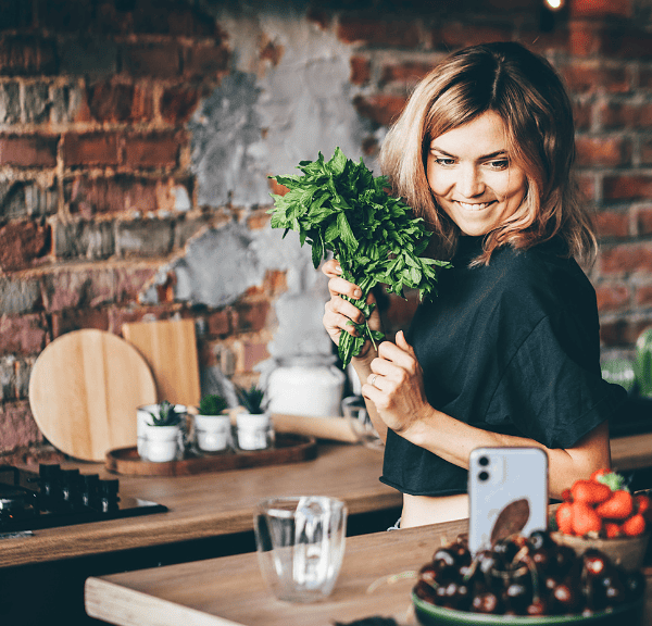 Woman joyfully holding fresh parsley in a rustic kitchen, embodying the spirit of meal planning with healthy, fresh ingredients.