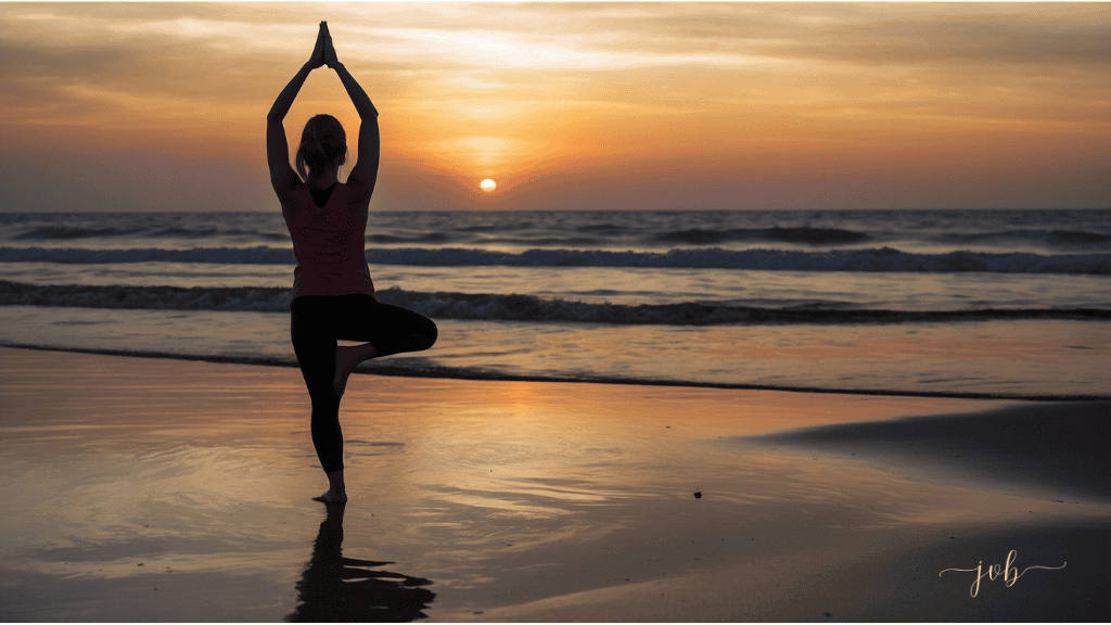 A woman practices a yoga tree pose on the beach at sunset, with her arms extended overhead, silhouetted against the setting sun and reflective ocean waters.