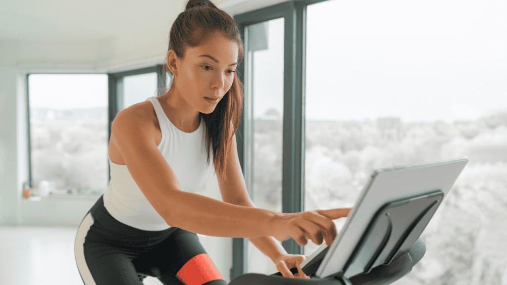 Focused woman adjusting a tablet on a stationary bike in a bright, modern home.