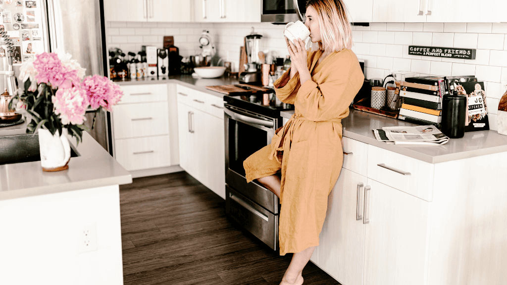 Woman in a luxurious robe enjoying coffee in a stylish kitchen.