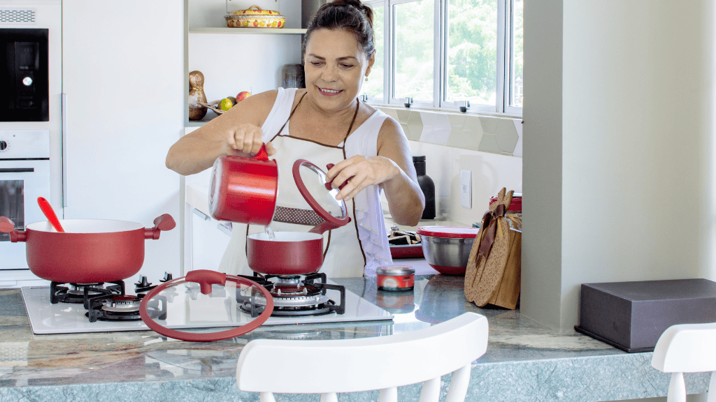 A woman cooking with red kitchenware in a modern kitchen.