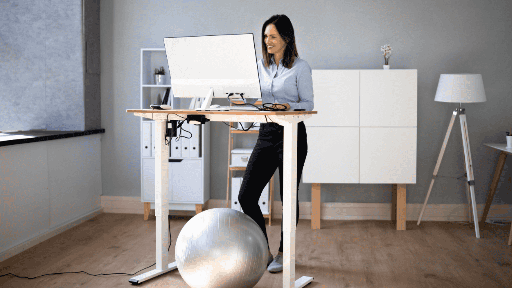 Woman using an adjustable standing desk with an ergonomic setup in a modern office.