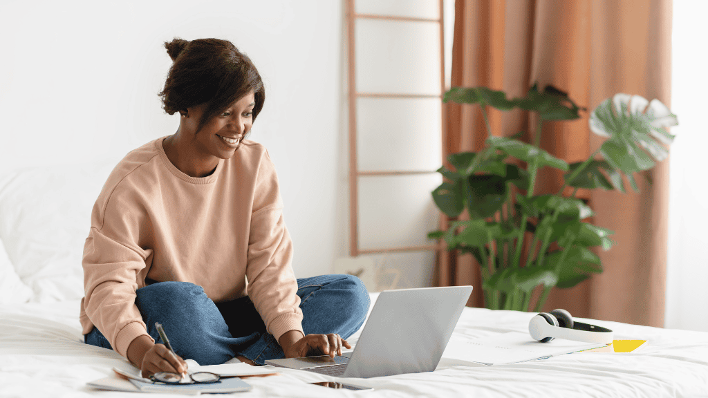 Young woman smiling while working on her laptop in a cozy, plant-filled room.