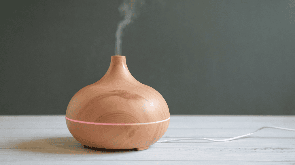 Wooden aromatherapy diffuser emitting steam on a white table against a gray wall.