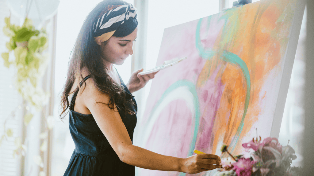 A woman painting on a canvas, surrounded by natural light and flowers.