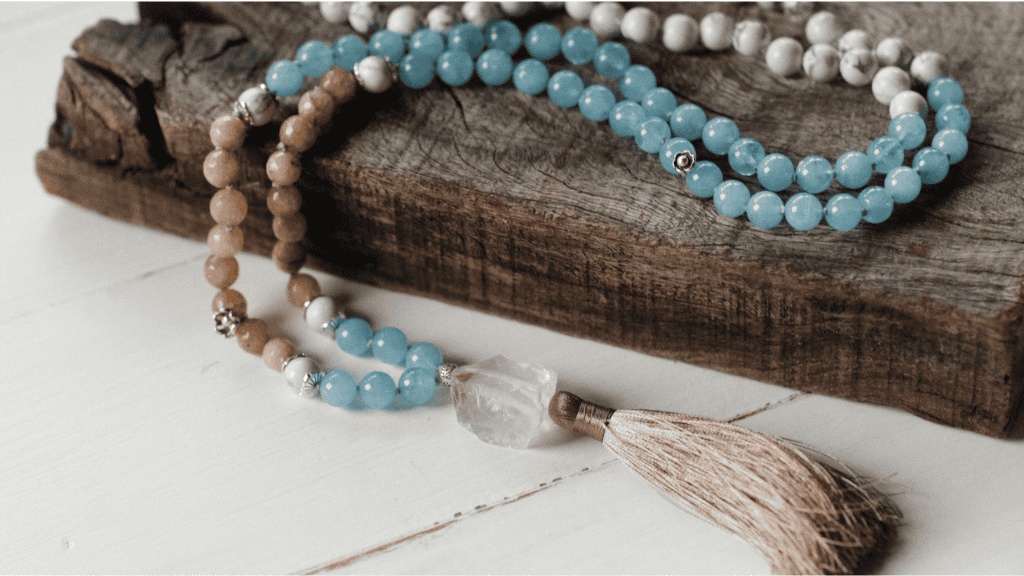 Prayer beads draped over a rustic wooden piece, featuring blue, beige, and white beads.