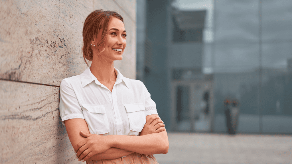 Confident, healthier woman leaning against a modern building wall, looking optimistically towards the distance.