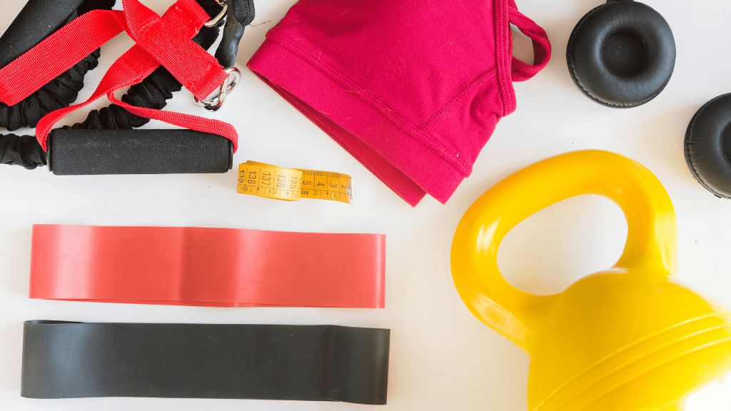 An assortment of essential fitness gear including resistance bands, a kettlebell, and workout gloves, laid out on a white background.