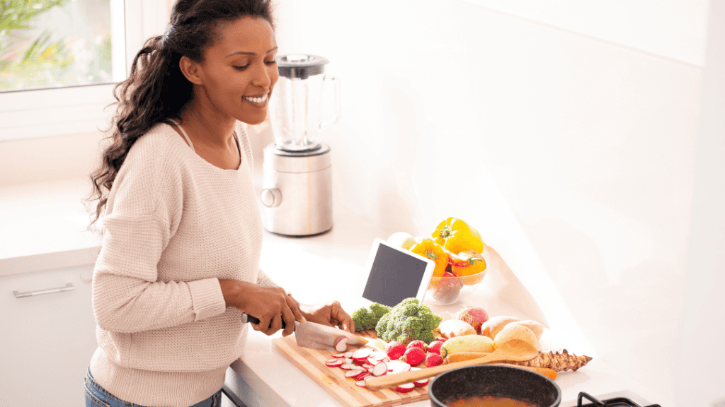 A woman joyfully preparing a variety of fresh vegetables in her bright kitchen, embodying healthy eating habits.