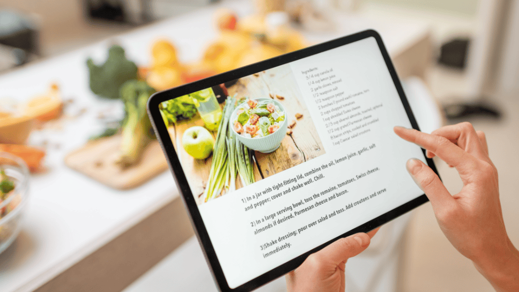 Close-up of hands browsing a recipe on a tablet with a colorful array of fresh ingredients in the background.