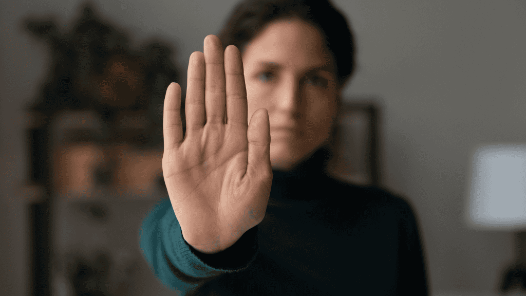 A woman holding her hand up in a stopping gesture, symbolizing the setting of personal boundaries.