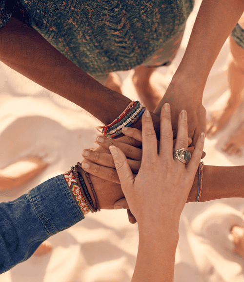 Diverse group of friends holding hands together in a circle on a sandy beach, symbolizing unity and support.