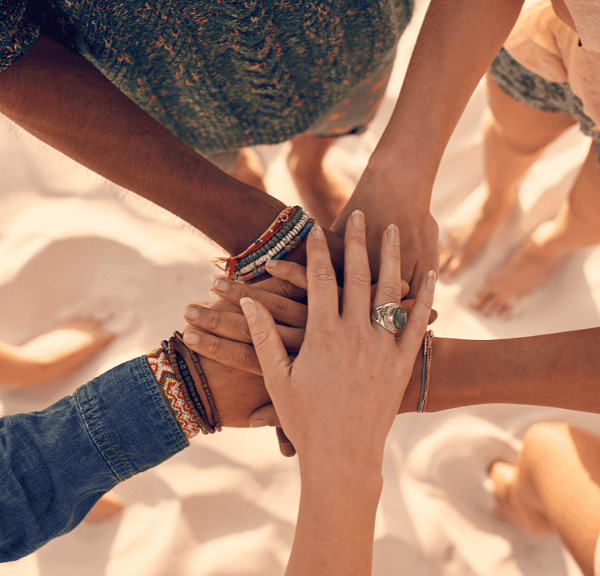 Diverse group of friends holding hands together in a circle on a sandy beach, symbolizing unity and support.