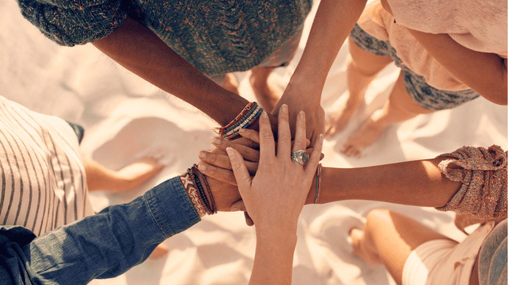 Diverse group of friends holding hands together in a circle on a sandy beach, symbolizing unity and support.