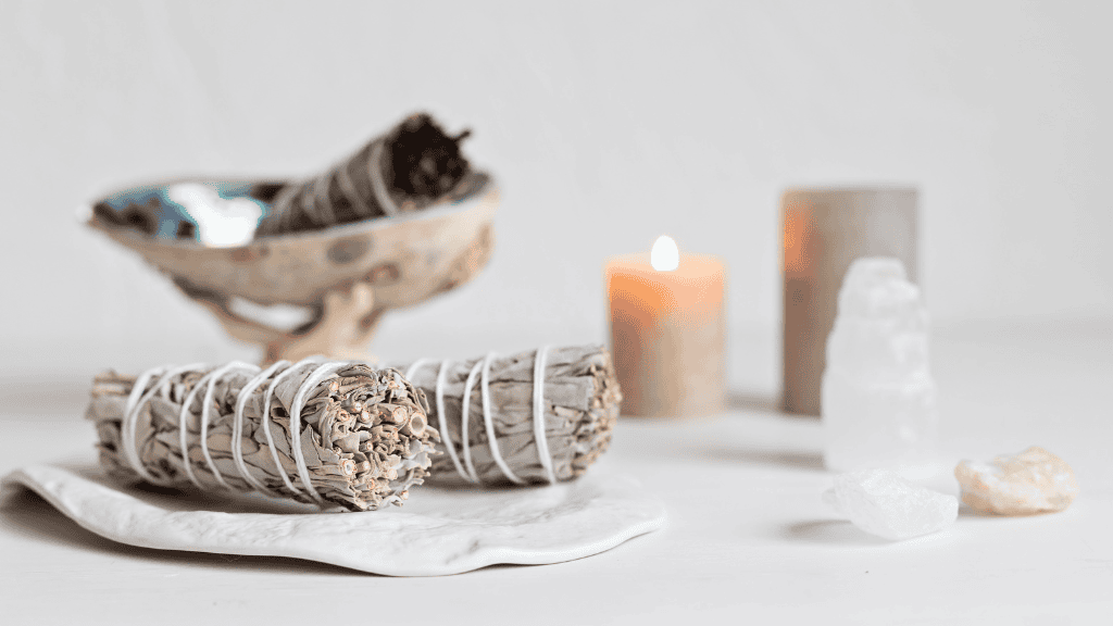 Elegant display of white sage bundles, a lit candle, and crystals on a serene background.