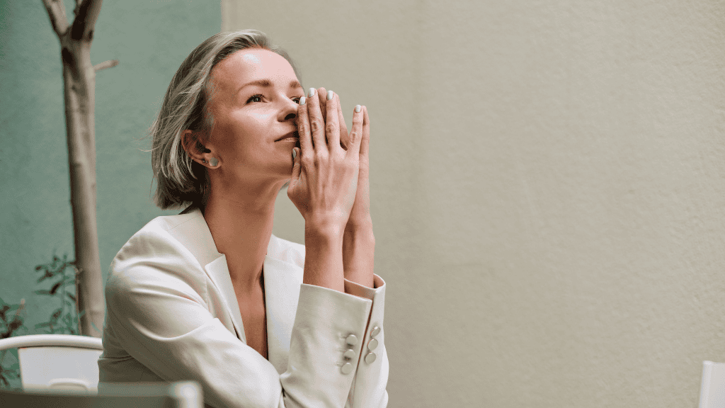 A thoughtful woman with closed eyes holds her hands together near her face.