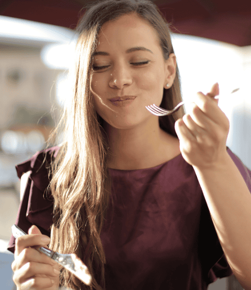 A young woman with a busy lifestyle mindfully enjoying her meal at an outdoor restaurant.