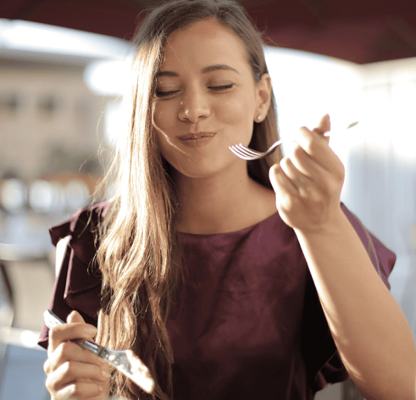 A young woman with a busy lifestyle mindfully enjoying her meal at an outdoor restaurant.