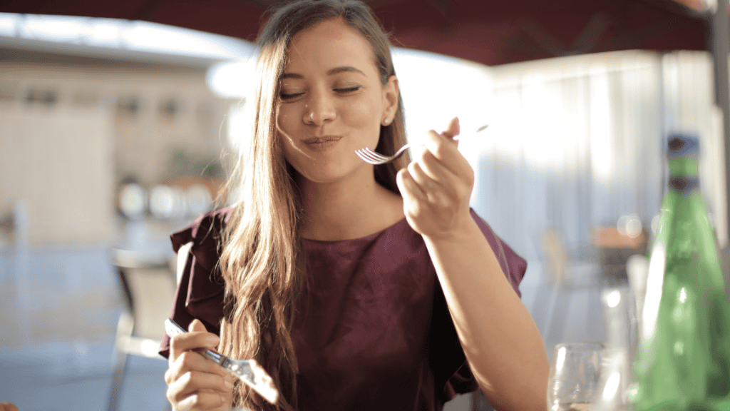 A young woman with a busy lifestyle mindfully enjoying her meal at an outdoor restaurant.