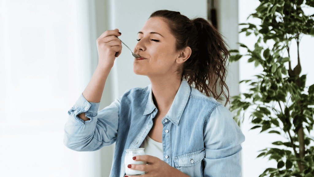 A woman in a denim jacket enjoying a glass of yogurt while looking pensively to the side.