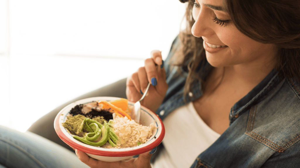 A smiling young woman eating a healthy meal of rice and vegetables from a bowl.