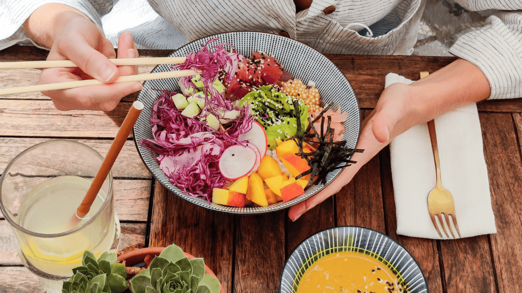 A table setting with a plate of colorful vegetables, a bowl of soup, and utensils on a rustic wooden surface.