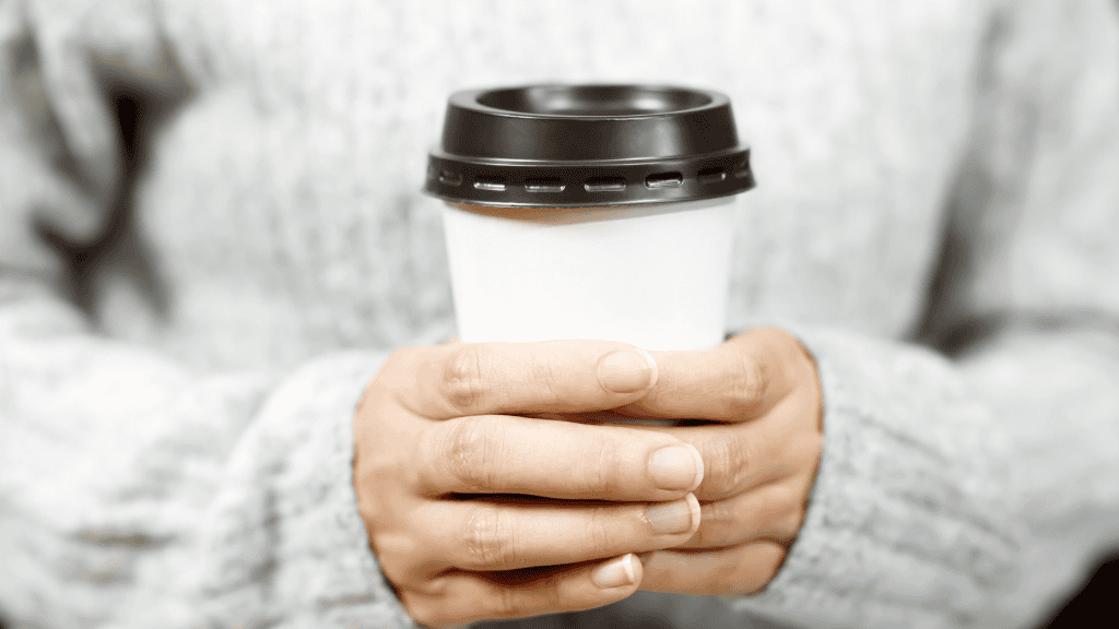 A close-up of hands holding a disposable coffee cup, with the cup lid visible.