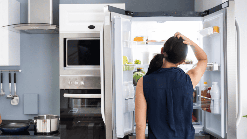 A person standing in front of an open refrigerator in a kitchen, reaching inside.