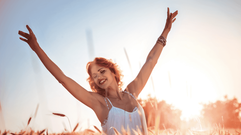 Joyful woman in a field at sunset, arms raised, embodying vitality and happiness through balanced nutrition.