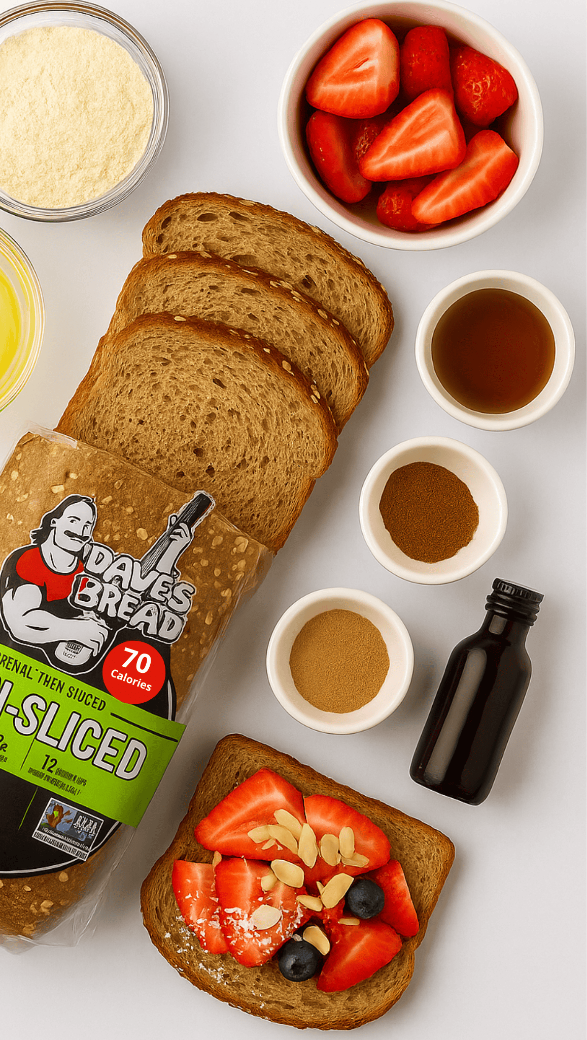 Sliced Dave’s Killer Bread topped with strawberries, blueberries, almond slivers, and coconut creates a healthy meal. Small bowls of strawberries, syrup, powders, vanilla extract, and grated cheese sit alongside on a white surface.