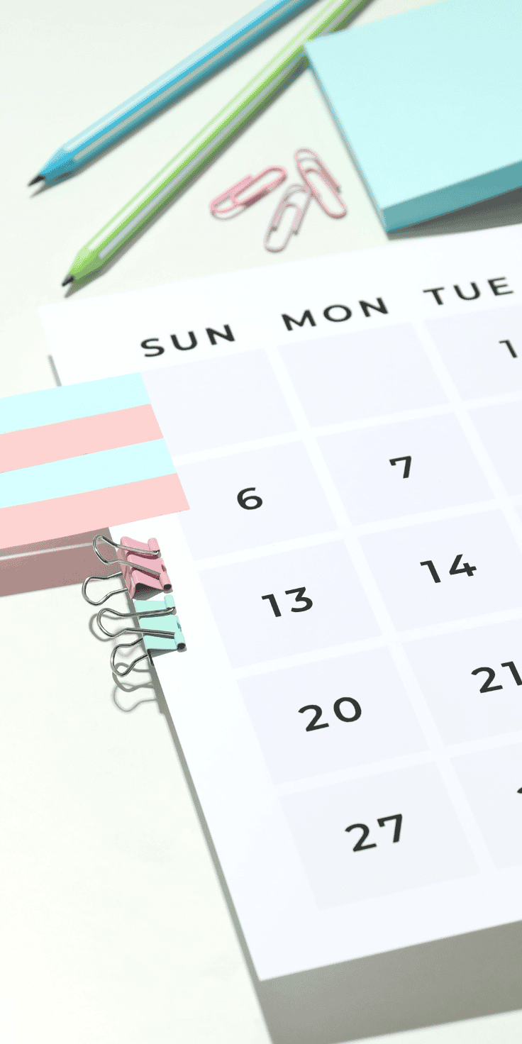 A calendar page lies on a desk with pastel-colored sticky notes labeled for a Diet Plan, binder clips, paper clips, and green and blue pencils arranged neatly beside it. The calendar shows part of a month.
