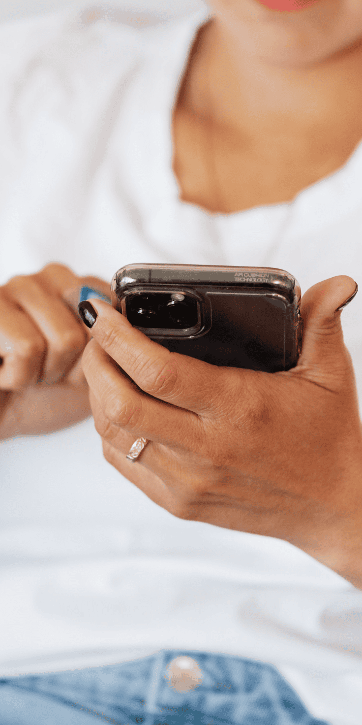 A person with painted nails and a ring on their finger is holding a smartphone, possibly checking their Diet Plan app, while wearing a white shirt.