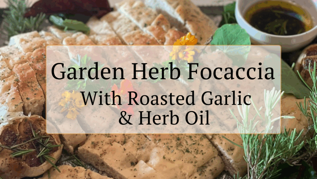 Sliced focaccia bread topped with herbs and edible flowers, served with a dish of herb oil and roasted garlic. Text overlay reads: “Garden Herb Focaccia With Roasted Garlic & Herb Oil.” Try this fresh focaccia recipe today.