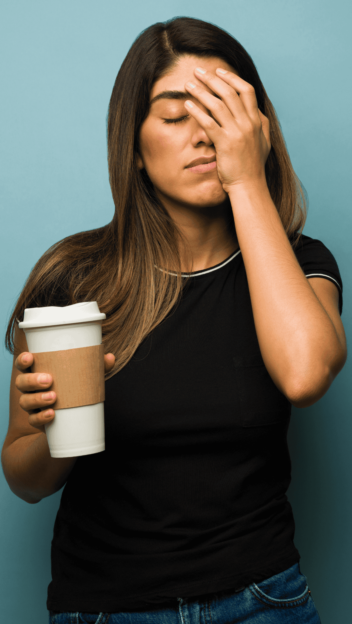 A woman in a black shirt holds a reusable coffee cup in one hand and covers her face with the other, appearing frustrated or tired—perhaps a sign of a stressed nervous system—against a plain blue background.
