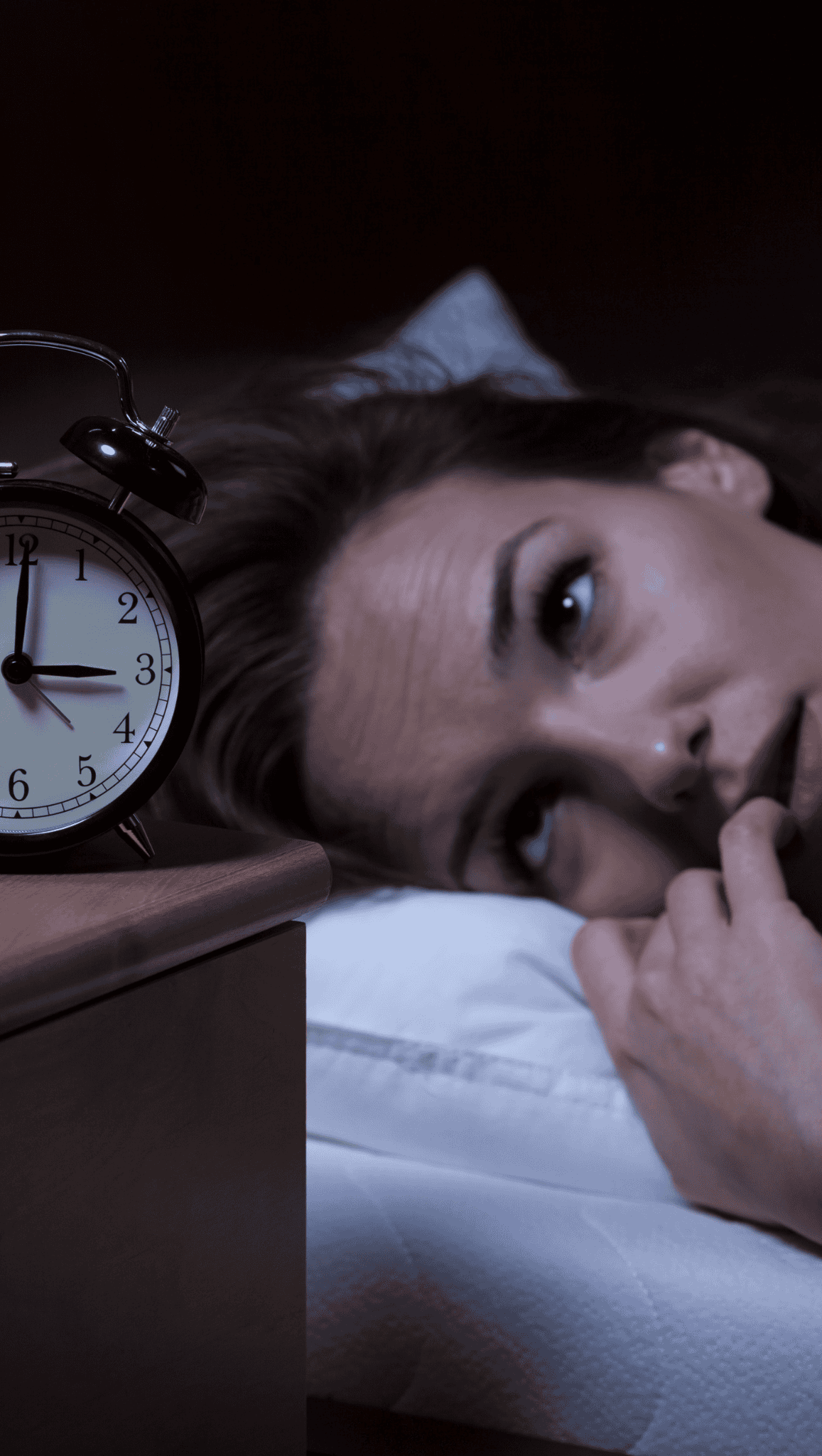 A woman lies in bed at night, looking worried and unable to sleep, her head on a pillow as the clock shows 2:45—her restless mind and overactive nervous system keeping her awake.